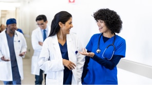 Two female doctors, one in a lab coat and the other in scrubs talking and walking together.